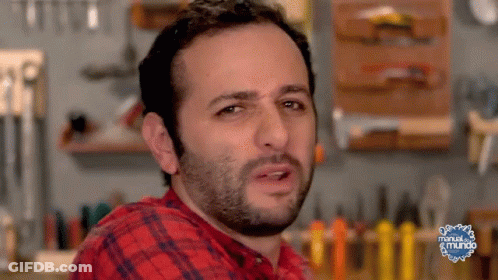 Man In Plaid Shirt Making Funny Face In Front Of Manual Del Mundo Sign GIF