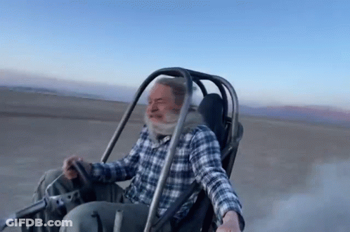 Man In Plaid Shirt Riding Buggy On Dirt Road GIF
