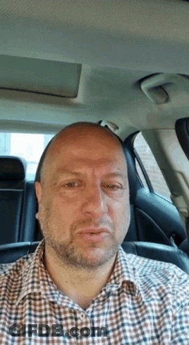 Man In Plaid Shirt Sitting In Car Looking At Camera GIF