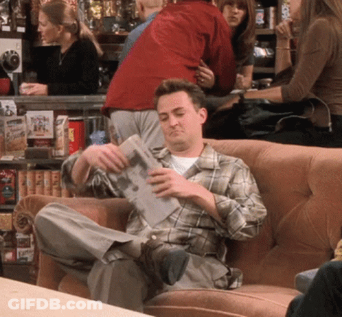 Man In Plaid Shirt Sitting On Couch Reading Paper GIF