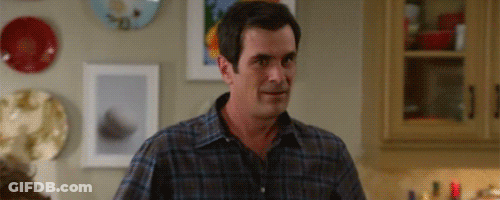 Man In Plaid Shirt Standing In Kitchen Looking At Something GIF