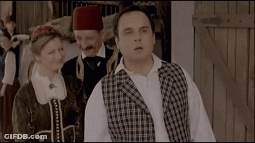 Man In Plaid Vest Beside Woman And Man In Turban GIF