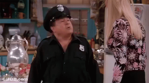 Man In Police Hat Talking To Woman In Kitchen GIF