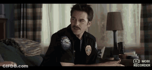 Man In Police Uniform With Mustache Sitting On Couch In Bedroom GIF