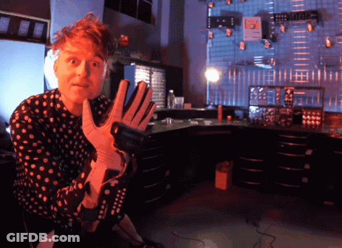 Man In Polka Dot Shirt Holding Gloves And Remote GIF