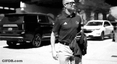 Man In Polo Shirt Walking While Holding Jacket And Looking At Phone GIF
