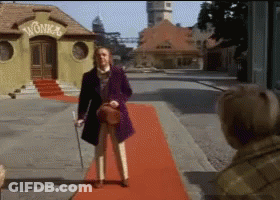 Man In Purple Coat On Red Carpet In Front Of Wonka Building GIF