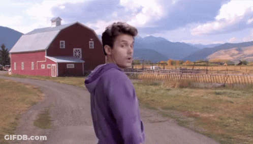 Man In Purple Hoodie Walking Down Dirt Road In Front Of Red Barn GIF