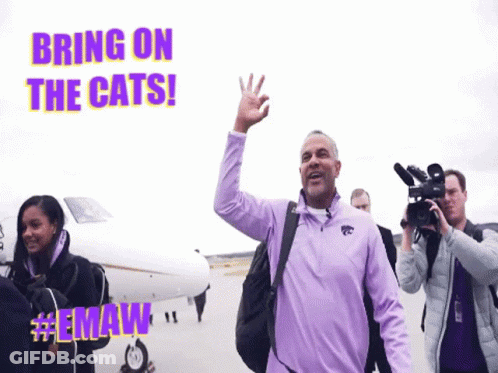 Man In Purple Jacket Waving In Front Of Plane Saying Bring On The Cats GIF