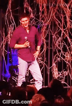 Man In Purple Shirt Holding Microphone On Stage GIF