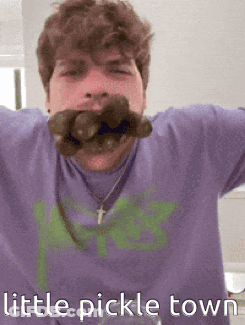 Man In Purple Shirt Holding Pickle In Mouth GIF