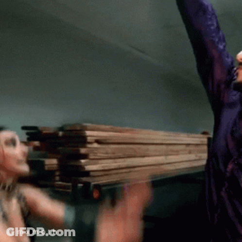 Man In Purple Shirt Holding Pile Of Wood GIF