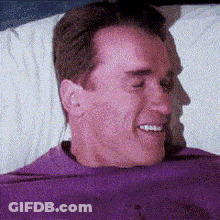 Man In Purple Shirt Laying On Bed Smiling GIF