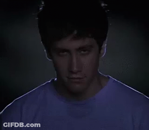 Man In Purple Shirt Looking At Camera In Dark GIF