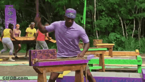 Man In Purple Shirt Standing Next To Wooden Table In Woods GIF