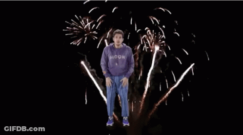 Man In Purple Sweatshirt Jumping In Front Of Fireworks GIF