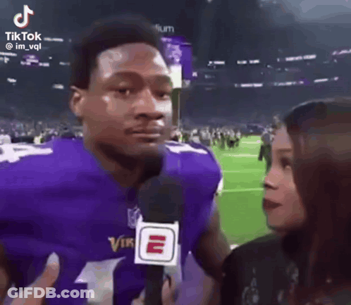 Man In Purple Vikings Jersey Talking To Woman With Microphone GIF
