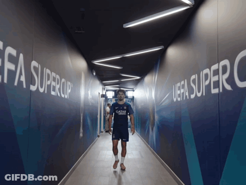 Man In Qatar Shirt Walking Through Hallway GIF