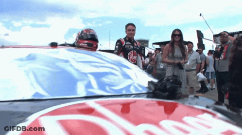Man In Race Car Standing Next To Woman In Dress GIF