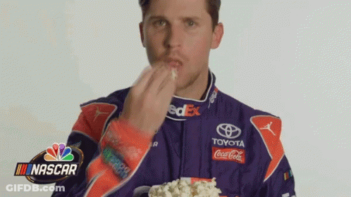 Man In Racing Suit Eating Popcorn From Cup GIF