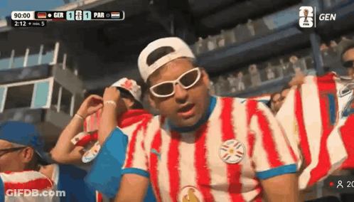 Man In Red And White Striped Shirt In Front Of Scoreboard GIF