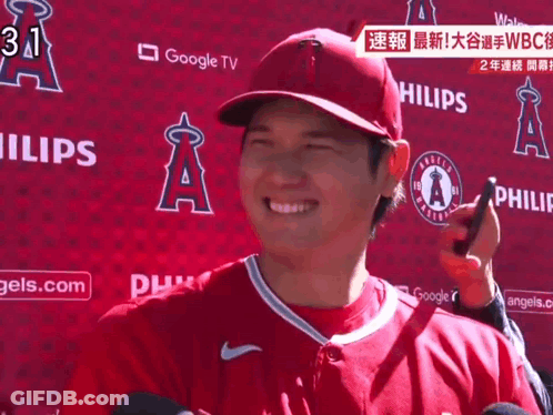 Man In Red Angels Jersey Smiling In Front Of Google TV Sign GIF