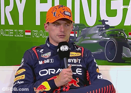 Man In Red Bull Jacket Holding Microphone In Front Of Ace 12 Race Sign GIF