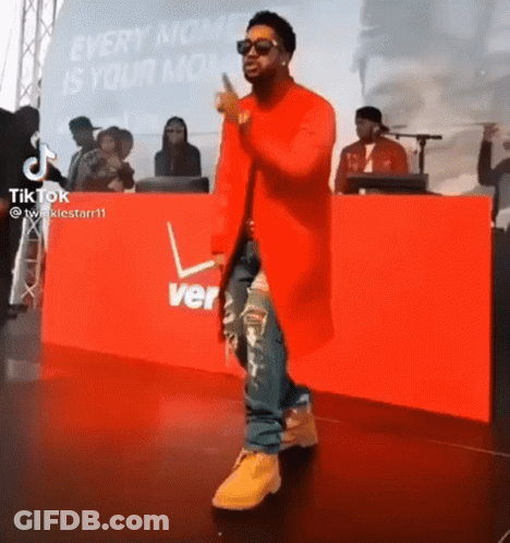Man In Red Coat On Stage In Front Of Verizon Sign GIF