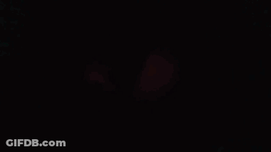 Man In Red Coat Staring At Camera In Dark Room GIF
