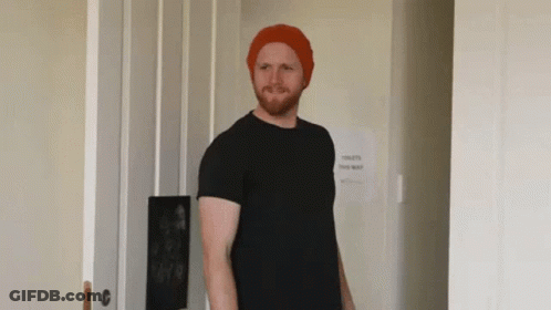 Man In Red Hat And Black Shirt In Front Of Toilets This Way Sign GIF