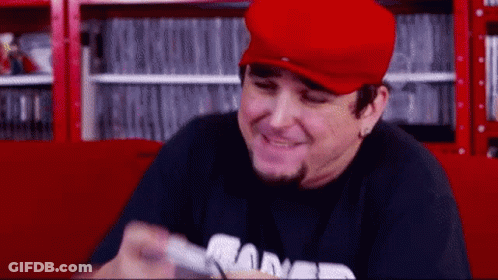 Man In Red Hat And Black Shirt Smiling Holding Remote GIF