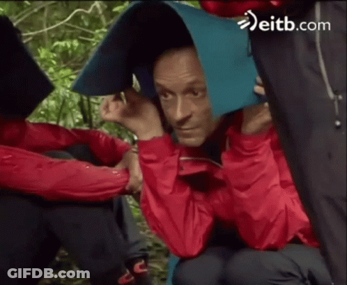 Man In Red Jacket Covering Head With Blue Blanket In Rain GIF