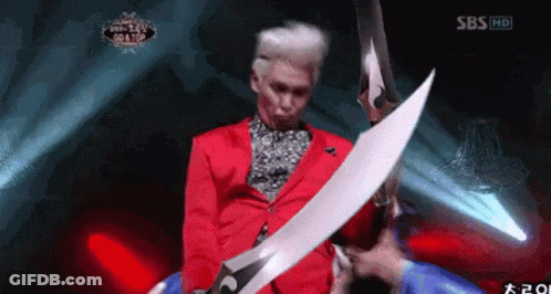Man In Red Jacket Holding Large Sword In Front Of SBS Logo GIF