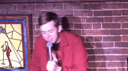 Man In Red Jacket Holding Microphone In Front Of Brick Wall GIF