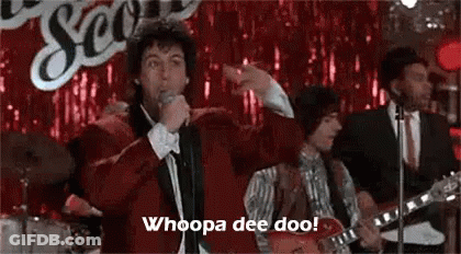 Man In Red Jacket Singing Into Microphone With Band GIF