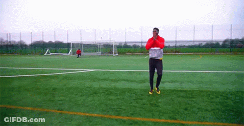 Man In Red Jacket Standing On Soccer Field With Goal GIF