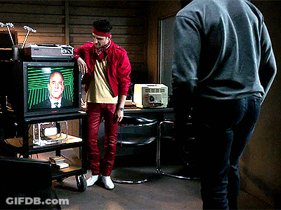 Man In Red Jacket Watching Man On TV GIF