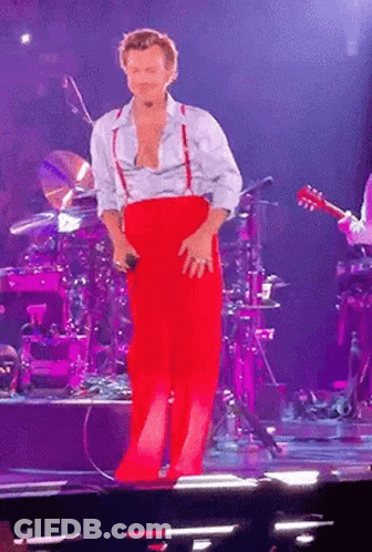 Man In Red Pants And Suspenders Standing On Stage GIF
