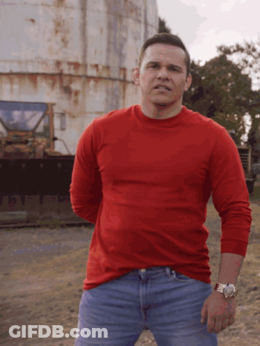 Man In Red Shirt And Blue Jeans In Front Of Rusty Silo GIF