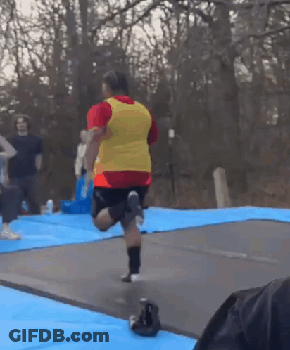 Man In Red Shirt And Yellow Vest Jumping On Trampoline GIF