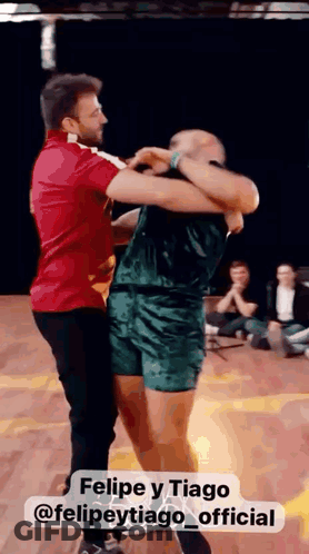 Man In Red Shirt Holding Man In Green Shorts Dancing GIF