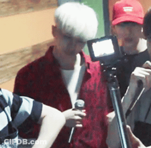 Man In Red Shirt Holding Microphone In Front Of Camera GIF