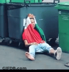 Man In Red Shirt Lying By Trash Cans GIF