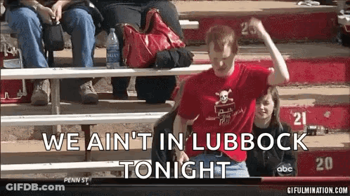 Man In Red Shirt Sitting On Bleacher Saying We Ain't In Lubbock Tonight GIF