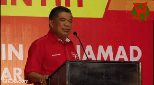 Man In Red Shirt Speaking At Podium In Jamad GIF