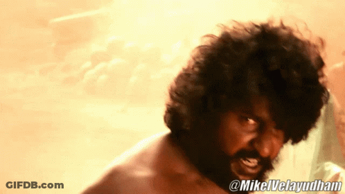 Man In Red Shirt Standing In Front Of Thatched Roof Building And Siriallu Sign GIF