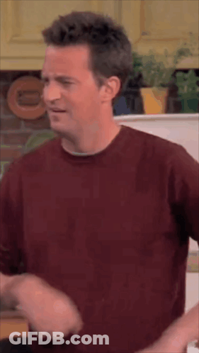 Man In Red Shirt Standing In Kitchen Making Funny Face GIF
