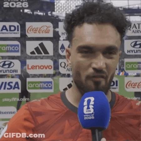 Man In Red Shirt Talking Into Blue Microphone With FIFA 2026 Logo GIF