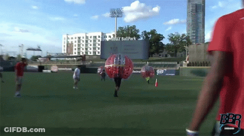 Man In Red Shirt Walking Past Ball Park Sign GIF