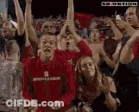 Man In Red Shirt With Letter S Surrounded By People GIF